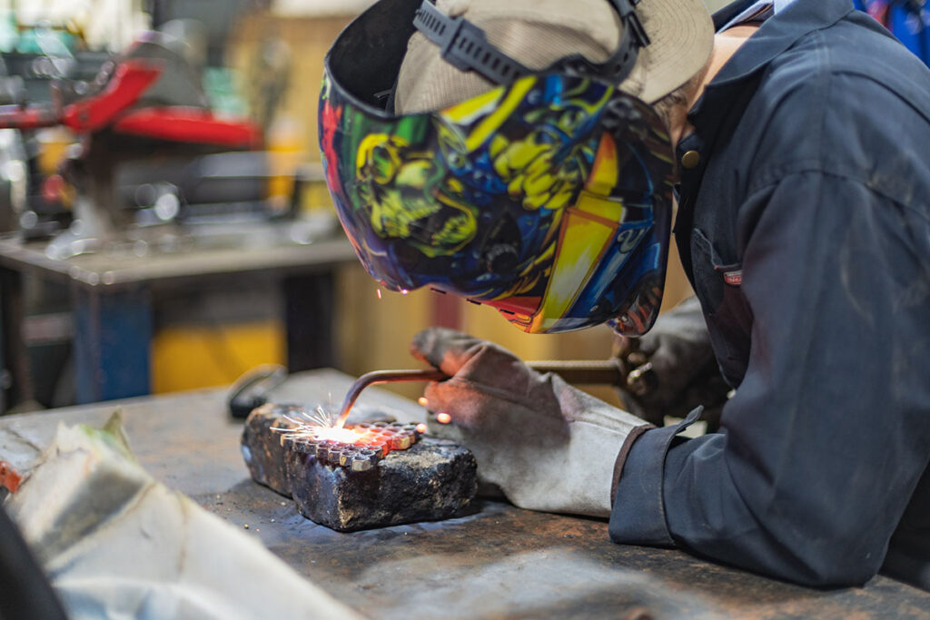 A welder in uniform works on a project in the metal shop.