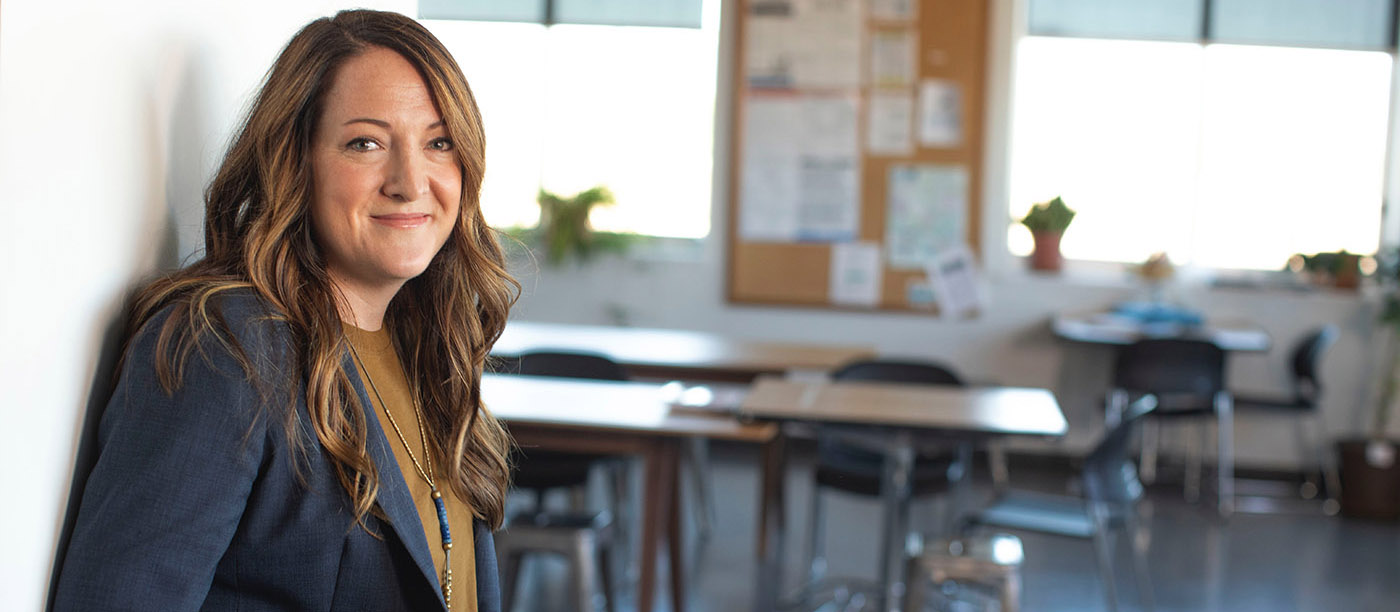 A teacher stands at the door of her classroom.