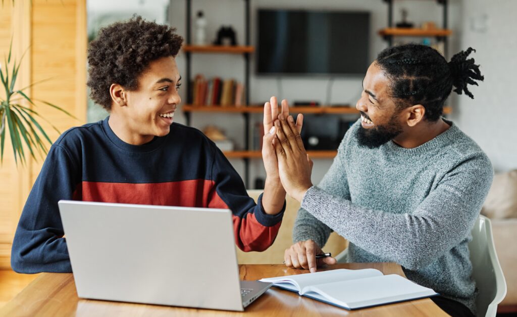 Two people smiling and laughing while high-fiving in front of a laptop